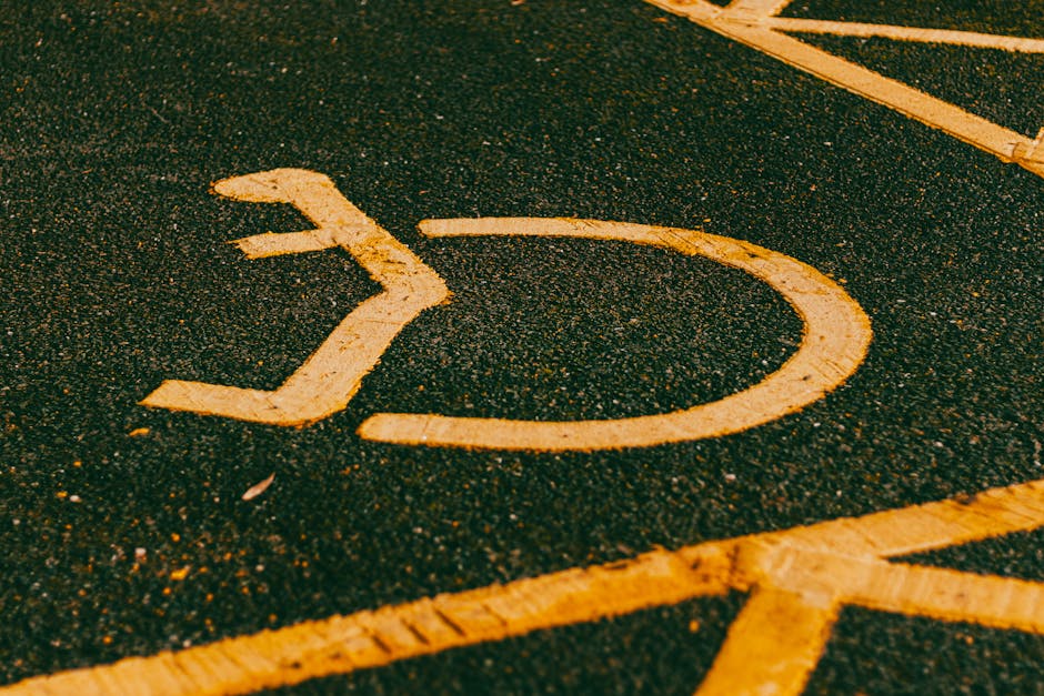 Close-up view of a wheelchair accessible parking space on a paved surface, with a yellow painted wheelchair symbol and surrounding yellow lines. The parking area appears to be outdoors under natural lighting, with asphalt texture visible beneath the paint. This image highlights designated accessible parking, often relevant for site access during house removals or relocations. The scene is unoccupied at the moment, and the focus is on the clear marking that ensures easy identification for individuals requiring accessible parking. For house removals, ensuring proper parking access with clear signage like this can facilitate smooth loading and unloading of furniture and boxes. Man with Van Locksbottom, specialists in removals, often assist clients in navigating parking regulations and access points for efficient moving logistics, as suggested by this type of parking space imagery.