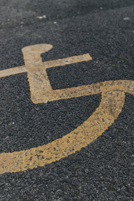 Close-up view of a wheelchair accessible parking space on a paved surface, with a yellow painted wheelchair symbol and surrounding yellow lines. The parking area appears to be outdoors under natural lighting, with asphalt texture visible beneath the paint. This image highlights designated accessible parking, often relevant for site access during house removals or relocations. The scene is unoccupied at the moment, and the focus is on the clear marking that ensures easy identification for individuals requiring accessible parking. For house removals, ensuring proper parking access with clear signage like this can facilitate smooth loading and unloading of furniture and boxes. Man with Van Locksbottom, specialists in removals, often assist clients in navigating parking regulations and access points for efficient moving logistics, as suggested by this type of parking space imagery.